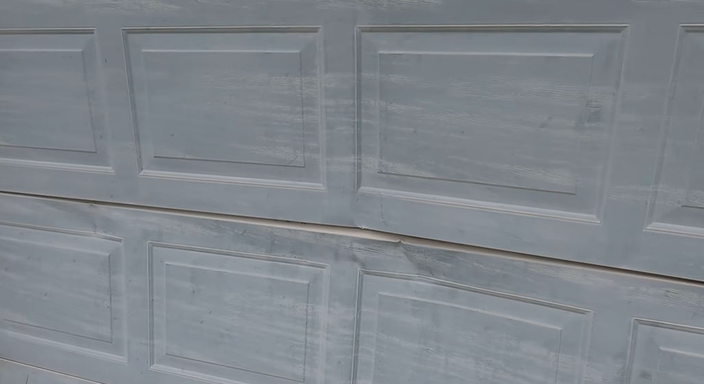 Close-up of a bent and damaged garage door panel seam